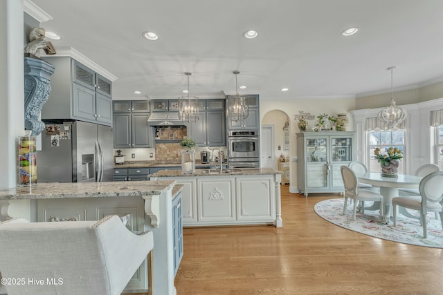 kitchen featuring light stone countertops, arched walkways, stainless steel appliances, and gray cabinetry