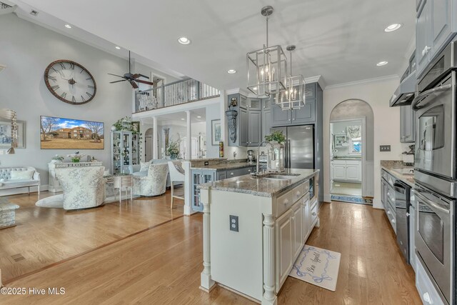 kitchen with a sink, light wood-style floors, open floor plan, gray cabinets, and light stone countertops