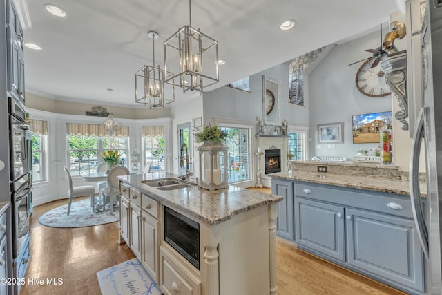 kitchen featuring a warm lit fireplace, appliances with stainless steel finishes, light wood finished floors, and a sink