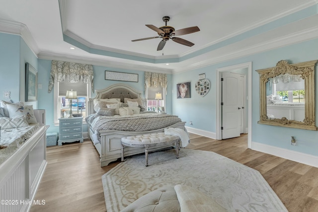 bedroom with light wood-style floors, a tray ceiling, ornamental molding, and baseboards