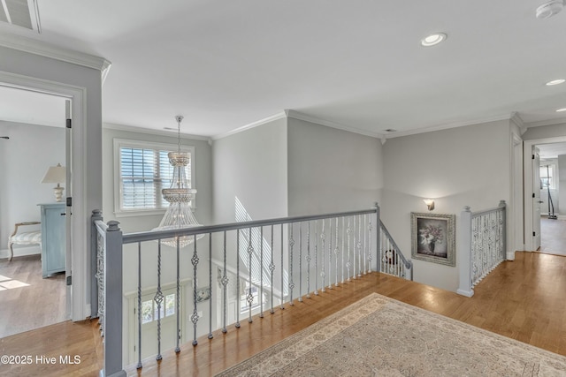 corridor with an inviting chandelier, ornamental molding, wood finished floors, and an upstairs landing