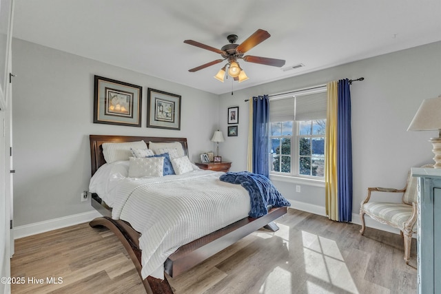 bedroom with a ceiling fan, visible vents, baseboards, and wood finished floors