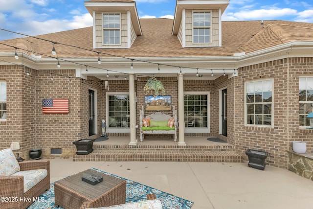 rear view of house featuring a shingled roof, crawl space, brick siding, and a patio