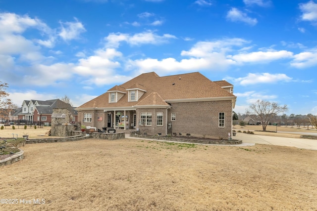 rear view of property with brick siding, roof with shingles, and a patio area