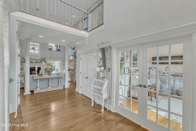 foyer entrance with a lit fireplace, a high ceiling, wood finished floors, and french doors