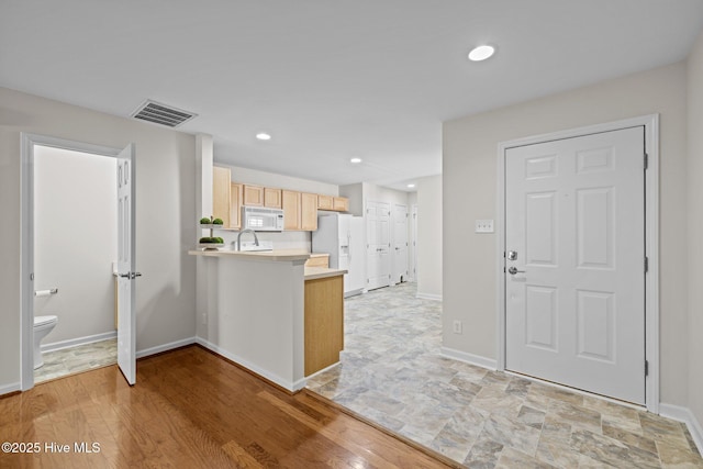 kitchen featuring white appliances, visible vents, a peninsula, light countertops, and light brown cabinets