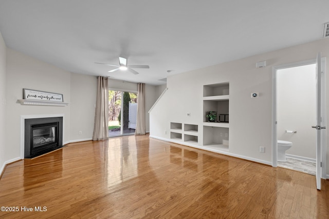 unfurnished living room with built in features, baseboards, a fireplace with flush hearth, and wood finished floors