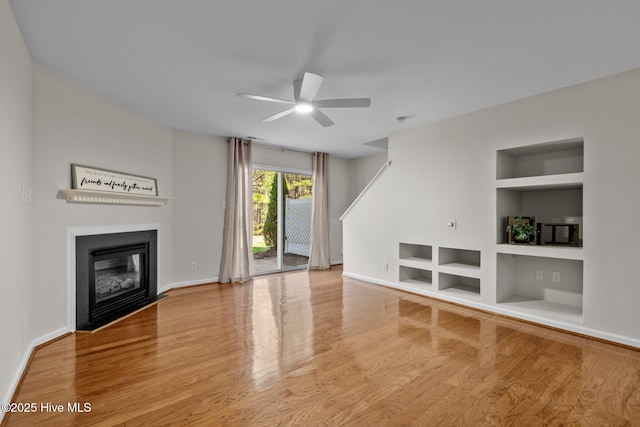 unfurnished living room with ceiling fan, a fireplace with flush hearth, wood finished floors, baseboards, and built in features