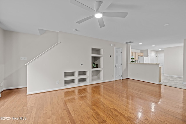 unfurnished living room featuring built in shelves, light wood finished floors, visible vents, a ceiling fan, and baseboards