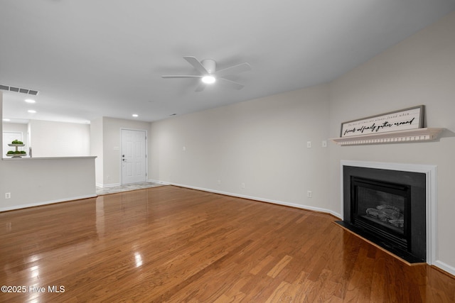 unfurnished living room with a glass covered fireplace, wood finished floors, visible vents, and a ceiling fan