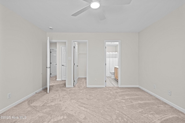 unfurnished bedroom featuring a closet, light colored carpet, a spacious closet, ensuite bath, and baseboards