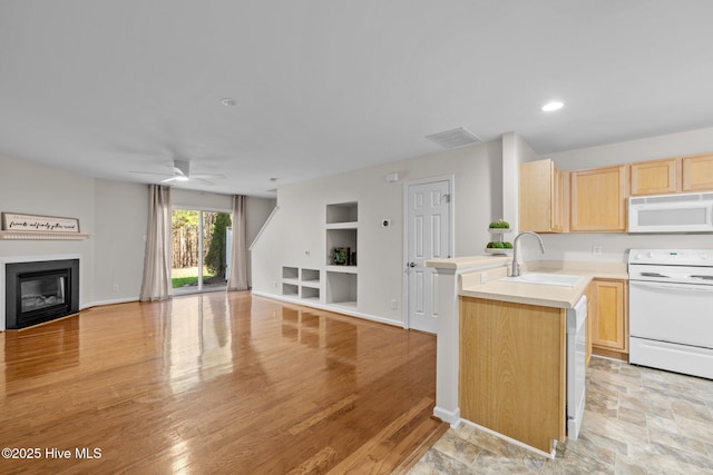 kitchen with light brown cabinets, a peninsula, white appliances, a sink, and open floor plan