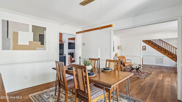 dining space featuring visible vents, crown molding, a fireplace, and wood finished floors