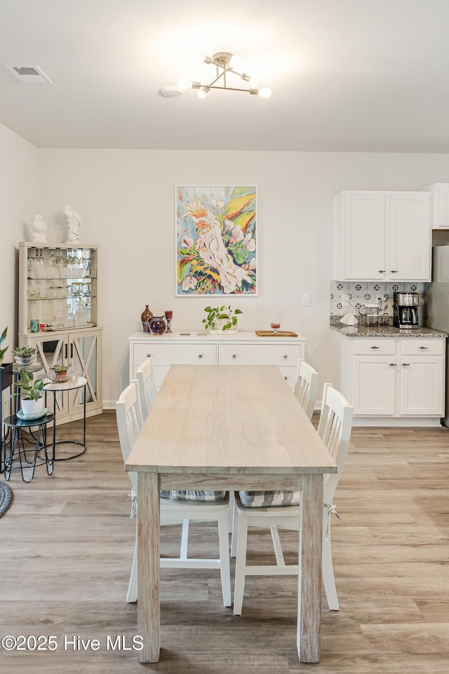 dining area with light wood-type flooring, visible vents, and baseboards