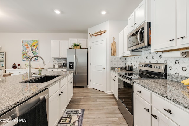 kitchen with white cabinets, light stone countertops, stainless steel appliances, and a sink