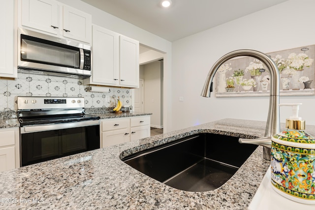 kitchen featuring stainless steel appliances, light stone counters, backsplash, and white cabinets