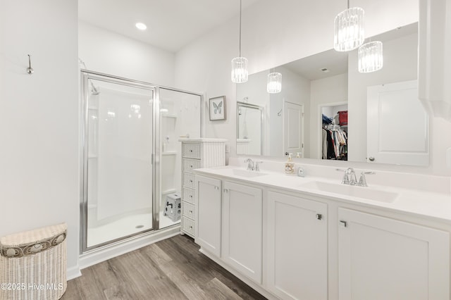 full bathroom featuring double vanity, wood finished floors, a spacious closet, a shower stall, and a sink