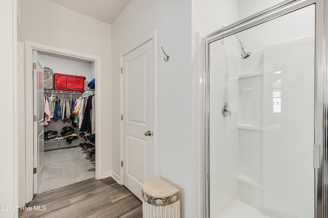 bathroom featuring a stall shower, a walk in closet, and wood finished floors