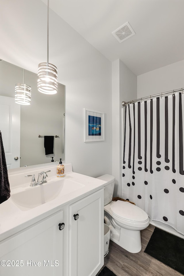 full bath featuring visible vents, a shower with shower curtain, toilet, wood finished floors, and vanity