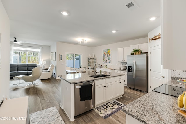 kitchen featuring an island with sink, appliances with stainless steel finishes, wood finished floors, white cabinetry, and a sink