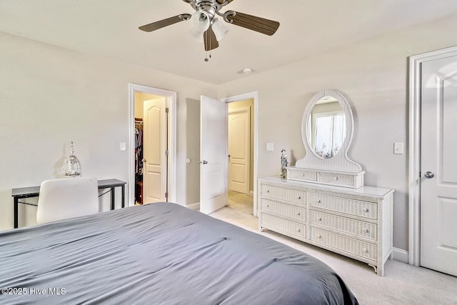 bedroom with a walk in closet, light carpet, ceiling fan, and baseboards