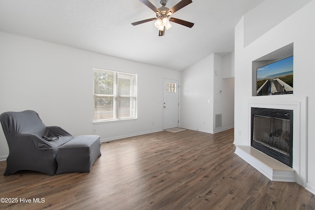 sitting room with visible vents, wood finished floors, a glass covered fireplace, baseboards, and vaulted ceiling