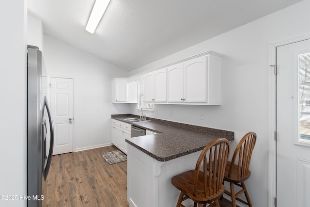 kitchen with a peninsula, a sink, vaulted ceiling, appliances with stainless steel finishes, and dark countertops