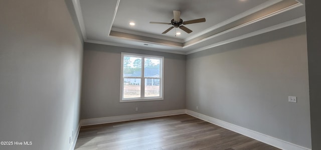 empty room with a raised ceiling, ornamental molding, ceiling fan, wood finished floors, and baseboards