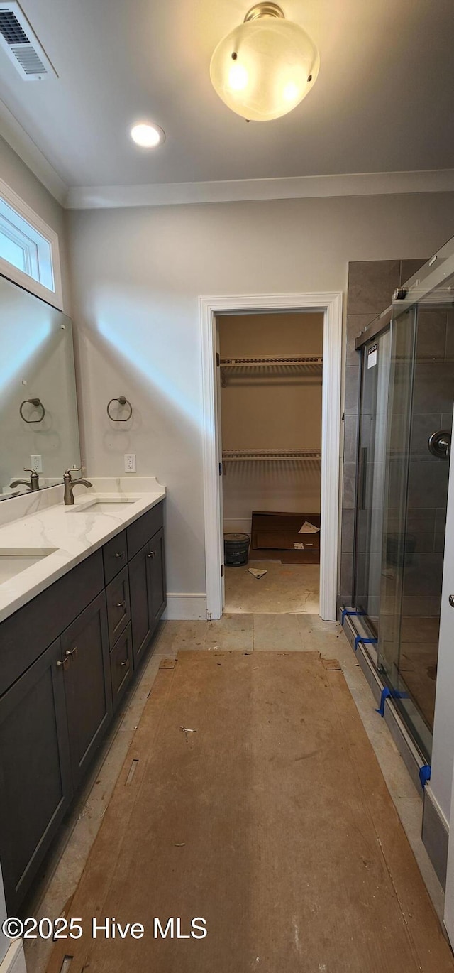 full bathroom with a stall shower, visible vents, ornamental molding, a walk in closet, and a sink