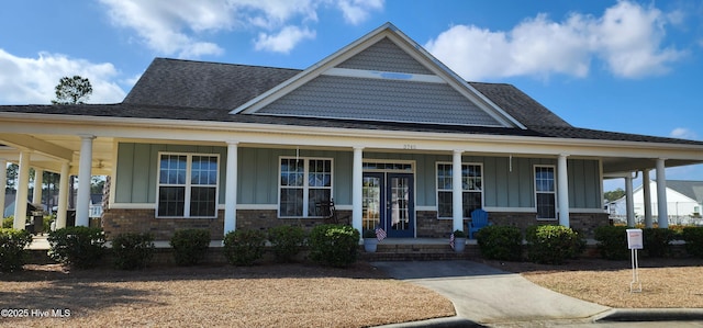 view of front facade with board and batten siding, covered porch, brick siding, and french doors