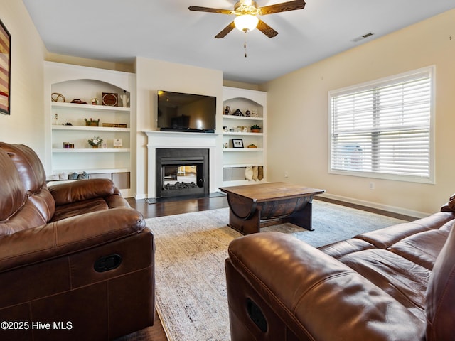 living area featuring built in shelves, visible vents, a multi sided fireplace, wood finished floors, and baseboards