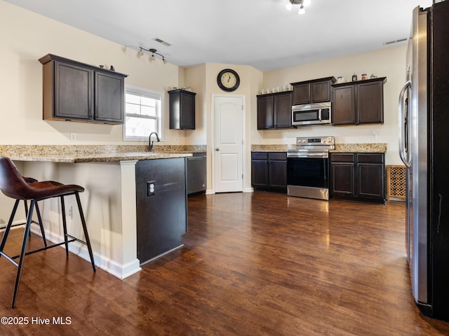 kitchen with dark brown cabinetry, visible vents, appliances with stainless steel finishes, dark wood-type flooring, and a peninsula