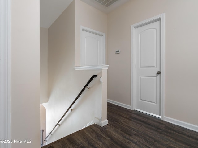 hall featuring baseboards, visible vents, dark wood finished floors, and an upstairs landing