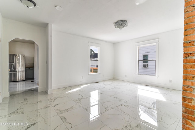 spare room with arched walkways, marble finish floor, and baseboards