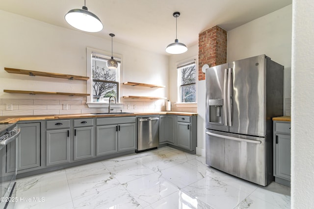 kitchen featuring appliances with stainless steel finishes, a sink, gray cabinetry, open shelves, and wooden counters