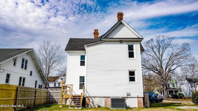 rear view of property featuring a shingled roof, central AC, fence, and a chimney