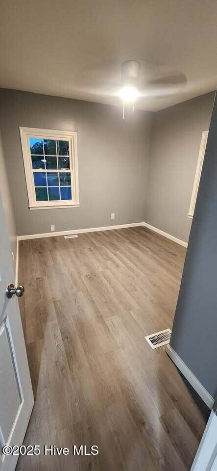 unfurnished room featuring wood finished floors, visible vents, and baseboards