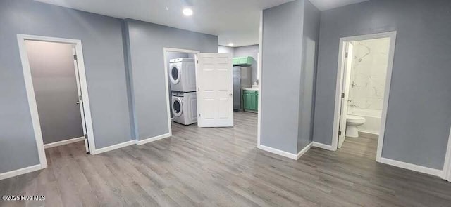 interior space with wood finished floors, stacked washer and clothes dryer, baseboards, and laundry area