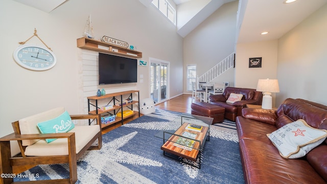 living area with recessed lighting, a high ceiling, wood finished floors, baseboards, and stairs