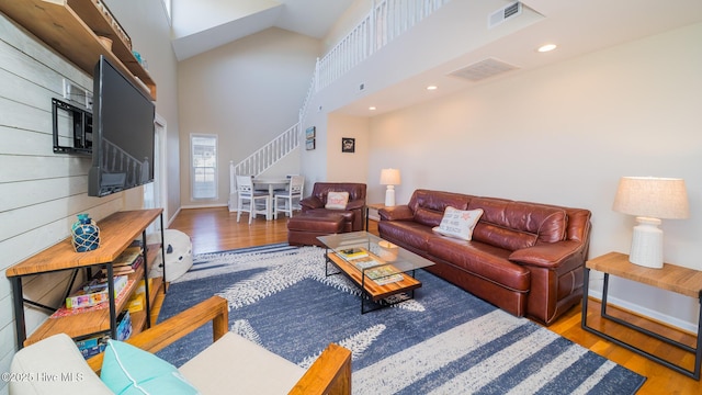 living room with high vaulted ceiling, stairway, visible vents, and wood finished floors