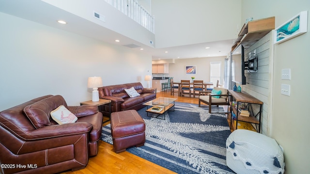 living room featuring a towering ceiling, light wood finished floors, visible vents, and recessed lighting