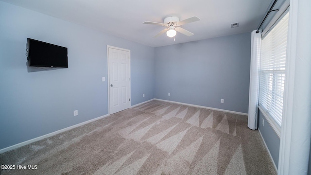 carpeted spare room featuring ceiling fan, visible vents, and baseboards