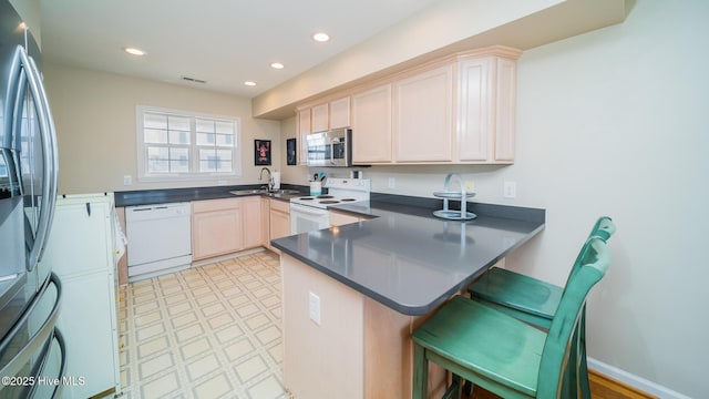 kitchen with dark countertops, appliances with stainless steel finishes, a breakfast bar, a peninsula, and a sink