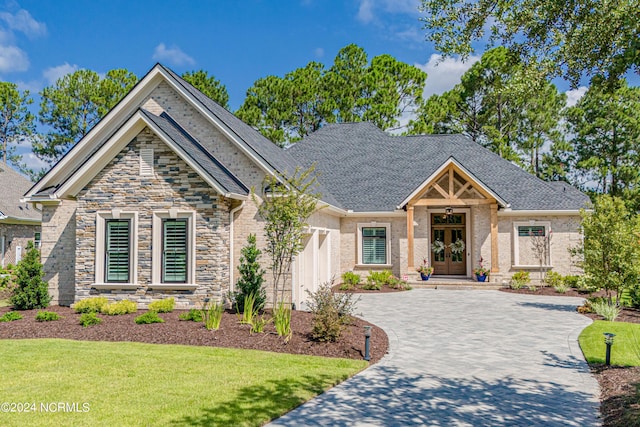 craftsman-style house featuring a garage, french doors, roof with shingles, decorative driveway, and a front lawn