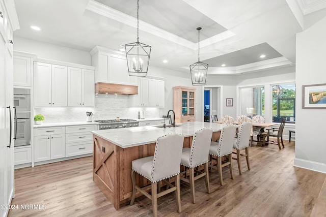 kitchen with a sink, light wood finished floors, a kitchen bar, and a raised ceiling