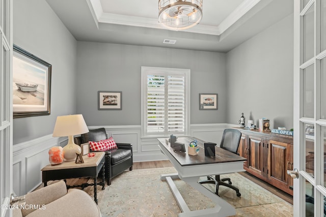 office space with a wainscoted wall, visible vents, a tray ceiling, and wood finished floors