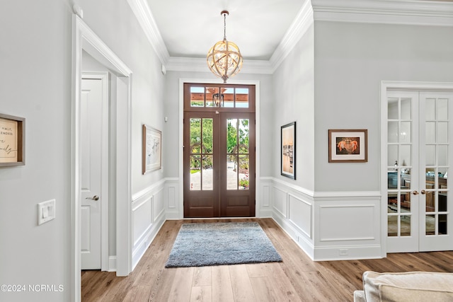 entryway with french doors, a wainscoted wall, a notable chandelier, light wood-style floors, and ornamental molding