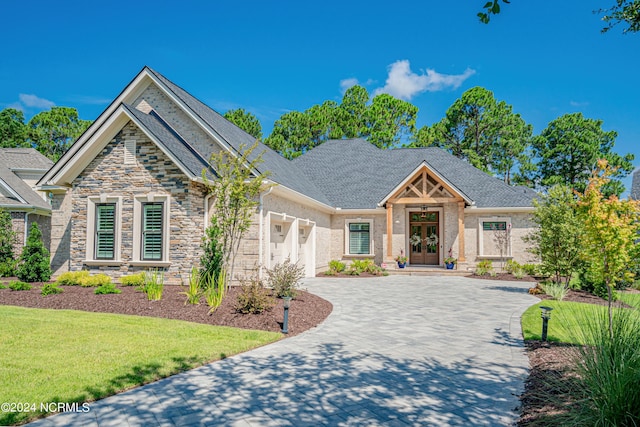 craftsman inspired home featuring driveway, a garage, stone siding, french doors, and a front yard