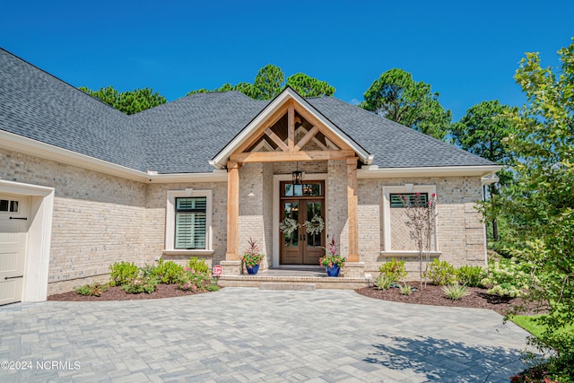 doorway to property featuring a shingled roof, french doors, and brick siding