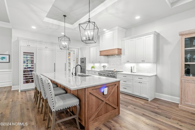 kitchen featuring a breakfast bar, stainless steel appliances, backsplash, light wood-style flooring, and a large island with sink